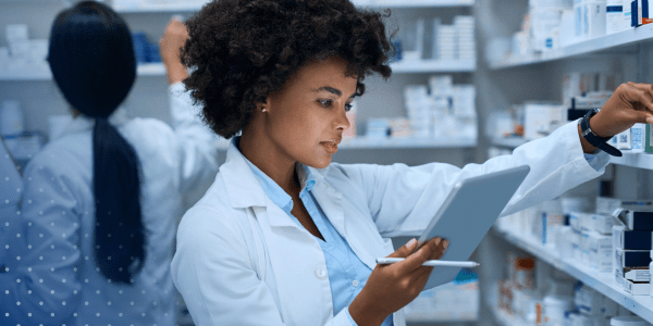 Pharmacist reading clipboard and picking product off shelf